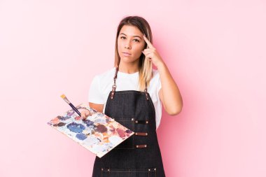 Kafkasyalı genç bir kadın, elinde bir palet ile tapınağı işaret ediyor, düşünüyor ve bir göreve odaklanıyor..