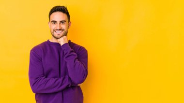 Sarı fırında izole edilmiş genç, mutlu ve kendinden emin gülümseyen, çenesine elleriyle dokunan beyaz bir adam..