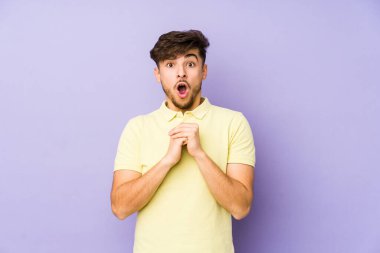 Mor bir arka planda izole edilmiş genç bir Arap adam şans diliyor, şaşırmış ve ağzı açık bir şekilde önüne bakıyor..