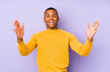 Mor arka planda izole edilmiş genç Latin bir adam hoş bir sürpriz alıyor, heyecanlı ve el kaldırıyor..