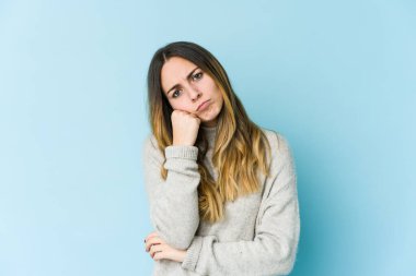 Mavi arka planda izole edilmiş, üzgün ve dalgın hisseden, kopyalama alanına bakan beyaz bir kadın..