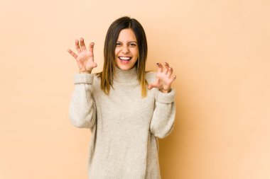 Bej arka planda izole edilmiş genç bir kadın pençelerini kedi taklidi yaparken gösteriyor, agresif bir hareket..