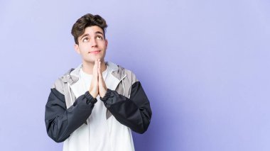 Mor arka planda izole olmuş genç beyaz bir adam el ele tutuşup, ağız kenarında dua ediyor, kendinden emin..