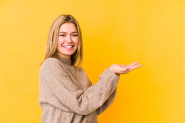 Sarı arka planda izole edilmiş genç sarışın bir kadın avucunun içinde bir kopya alanı tutuyor..