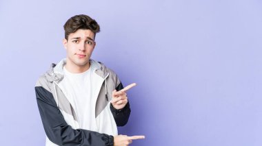 Mor arka planda izole edilmiş genç beyaz adam işaret parmağıyla fotokopi alanını işaret ederek şok oldu..