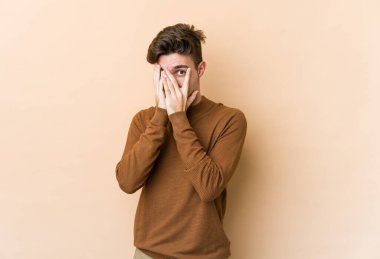 Beyazlı genç bir adam bej arka planda izole edilmiş. Korkmuş ve gergin parmaklarıyla göz kırp..