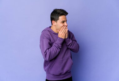 Mor arka planda izole olmuş genç beyaz bir adam bir şeye gülüyor, elleriyle ağzını kapatıyor..