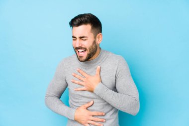 Mavi bir geçmişi olan beyaz bir genç mutlu bir şekilde gülüyor ve ellerini karnının üstünde tutarak eğleniyor..