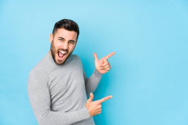 Mavi arka planda genç beyaz bir adam izole edilmiş, işaret parmaklarıyla bir fotokopi alanını işaret ediyor, heyecan ve arzuyu ifade ediyor..