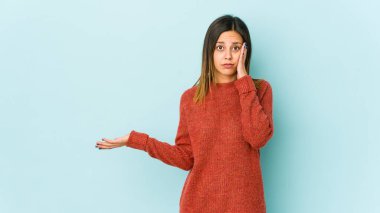 Mavi arka planda izole edilmiş genç bir kadın, avuç içinde kopya alanı tutmaktan etkilenmiş..