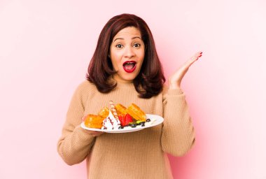 Orta yaşlı, elinde waffle tutan Latin kadın şaşırdı ve şok oldu..