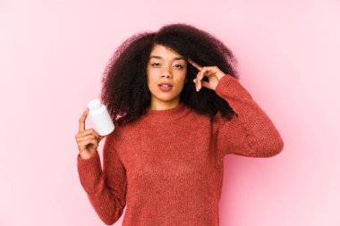 Vitaminlerini tutan genç afro bir kadın. Elinde vitamin bozan bir tapınak tutan genç bir afro kadın. Düşünüyor, bir göreve odaklanıyor..