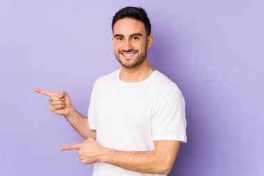 Mor arka planda izole edilmiş genç beyaz adam işaret parmağıyla işaret ederek heyecanlanıyor..