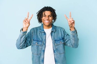 Kot pantolon giyen genç siyah adam zafer işareti gösteriyor ve gülümsüyor..