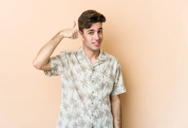 Beyazlı genç bir adam bej arka planda izole edilmiş. Elle bir gömlek fotokopi alanını işaret ediyor. Gururlu ve kendinden emin.