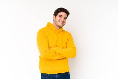 Beyaz arka planda kendini güvende hisseden, kararlılıkla kollarını kavuşturan genç adam..