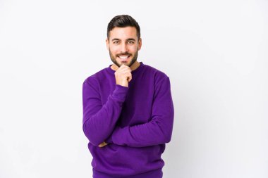 Beyaz arka planda genç beyaz bir adam izole edilmiş mutlu ve kendinden emin gülümseyen, elleriyle çeneye dokunan.