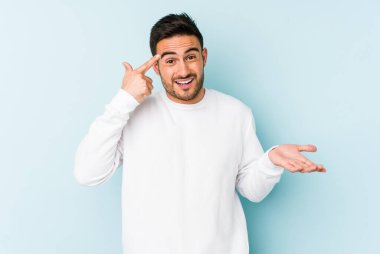 Mavi arka planda izole edilmiş genç beyaz adam işaret parmağıyla bir hayal kırıklığı jesti gösteriyor..
