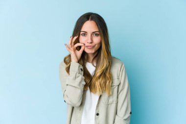 Mavi arka planda izole edilmiş genç beyaz kadın parmakları dudaklarında bir sır saklıyor..