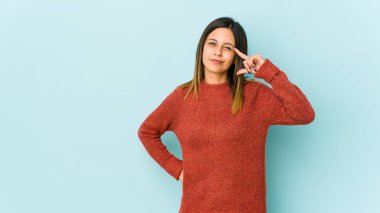 Mavi arka planda izole edilmiş genç bir kadın şakağı parmağıyla işaret ediyor, düşünüyor ve bir göreve odaklanıyor..