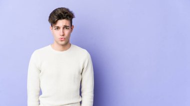 Mor arka planda izole edilmiş genç beyaz adamın yanakları şişer, yorgun bir ifadesi vardır. Yüz ifadesi kavramı.