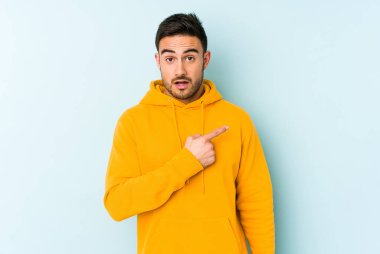 Mavi arka planda izole edilmiş genç beyaz adam yan tarafı işaret ediyor.