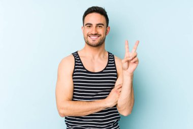 Mavi arka planda izole edilmiş genç beyaz adam iki numarayı parmaklarıyla gösteriyor..
