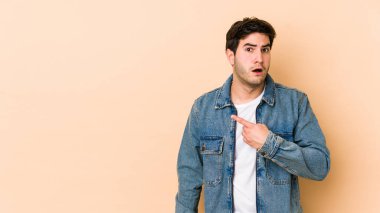 Bej arka planda izole edilmiş genç adam yan tarafı işaret ediyor.