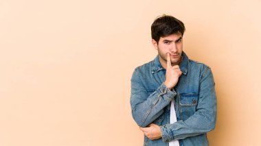 Bej arka planda izole edilmiş genç adam şüpheli ve şüpheci bir ifadeyle yana bakıyor..