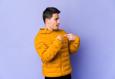 Mor arka planda izole edilmiş genç beyaz adam parmağını göstererek şaşırdı, geniş bir gülümsemeyle..