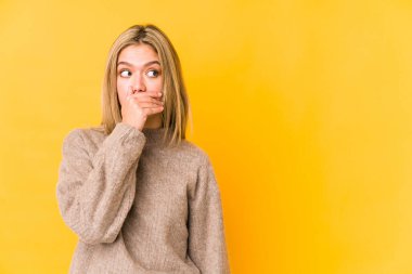 Sarışın genç kadın sarı arka planda izole edilmiş. Düşünceli bir şekilde bir fotokopi odasına bakıyor. Ağzını eliyle kapatıyor..