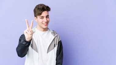 Mor arka planda izole edilmiş genç beyaz adam iki numarayı parmaklarıyla gösteriyor..