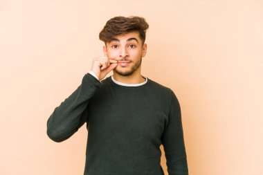 Bej bir arka planda izole edilmiş genç bir Arap adam parmakları dudaklarında bir sır saklıyor..