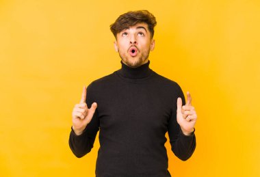 Sarı arka planda izole edilmiş genç bir Arap, ağzı açık, üst tarafı işaret ediyor..