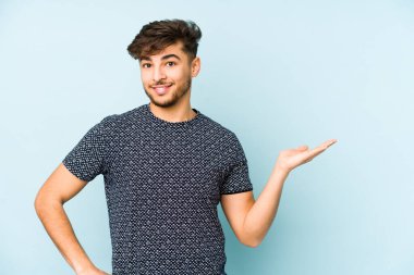 Mavi arka planda izole edilmiş genç bir Arap, avuç içinde bir kopya alanı ve belinde bir el daha olduğunu gösteriyor..