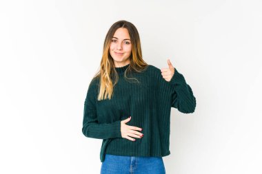 Beyaz arka planda izole genç beyaz kadın karnına dokunuyor, nazikçe gülümsüyor, yemek yiyor ve tatmin oluyor..