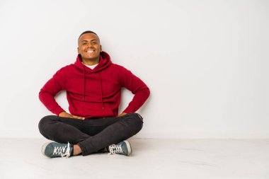 Yerde yalnız başına oturan genç latin adam ellerini kalçasından ayırmıyor..