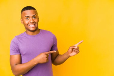 Sarı arka planda izole edilmiş genç latin adam işaret parmağıyla fotokopi alanını işaret ederek şok oldu..