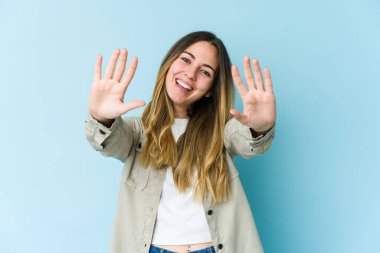 Mavi arka planda izole edilmiş genç beyaz kadın on numarayı elleriyle gösteriyor..