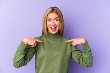 Sarışın, beyaz tenli, izole bir kadın. Parmakla işaret ederek şaşırmış, gülümseyerek..