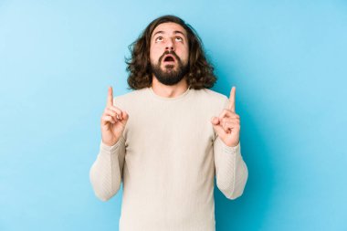 Mavi arka planda izole edilmiş, ağzı açık, üst tarafı gösteren genç, uzun saçlı adam..