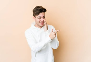 Beyaz tenli genç adam bej arka planda izole edilmiş. Dedikodu yapıyor, bir şeyleri bildiriyor..