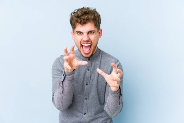 Sarışın, kıvırcık saçlı, beyaz tenli bir adam pençelerini kedi taklidi yaparken gösteriyor. Saldırgan bir hareket..