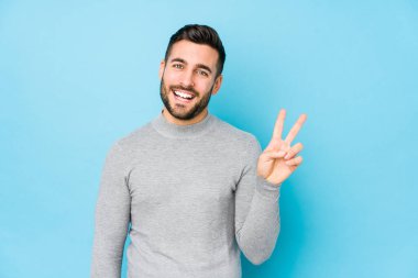 Mavi arka planda yaşayan beyaz bir adam neşeli ve tasasız bir şekilde parmaklarıyla barış sembolü gösteriyor..
