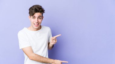 Mor arka planda izole edilmiş genç beyaz adam işaret parmağıyla işaret ederek heyecanlanıyor..