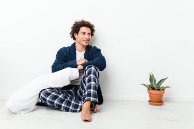 Olgun bir adam pijamasını giymiş evde oturmuş kollarını kavuşturup gülümsüyor..