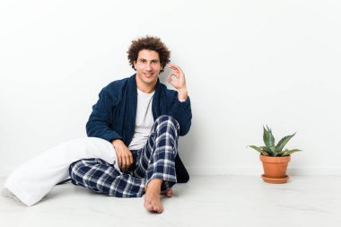 Olgun bir adam pijamasını giymiş, neşeli ve kendinden emin bir şekilde evde oturuyor..