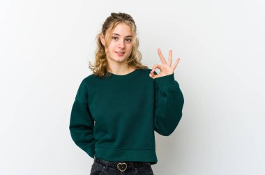 Beyaz arka plandaki genç beyaz kadın göz kırpıyor ve elleriyle iyi bir jest yapıyor..