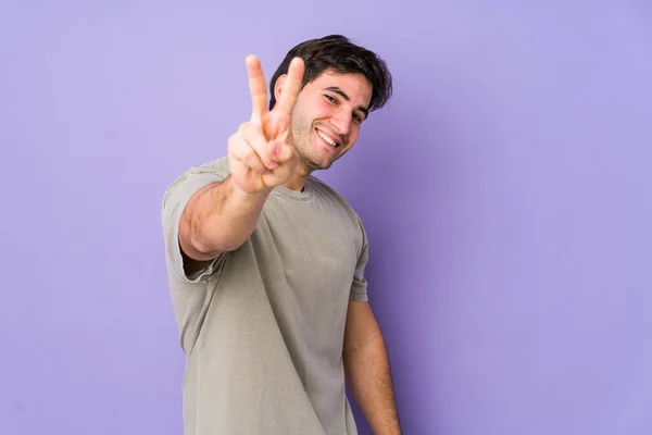 紫色の背景に孤立した若い男喜びと屈託のない指で平和のシンボルを示す — ストック写真