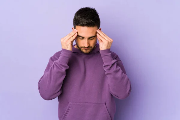 Young caucasian man isolated on purple background touching temples and having headache.